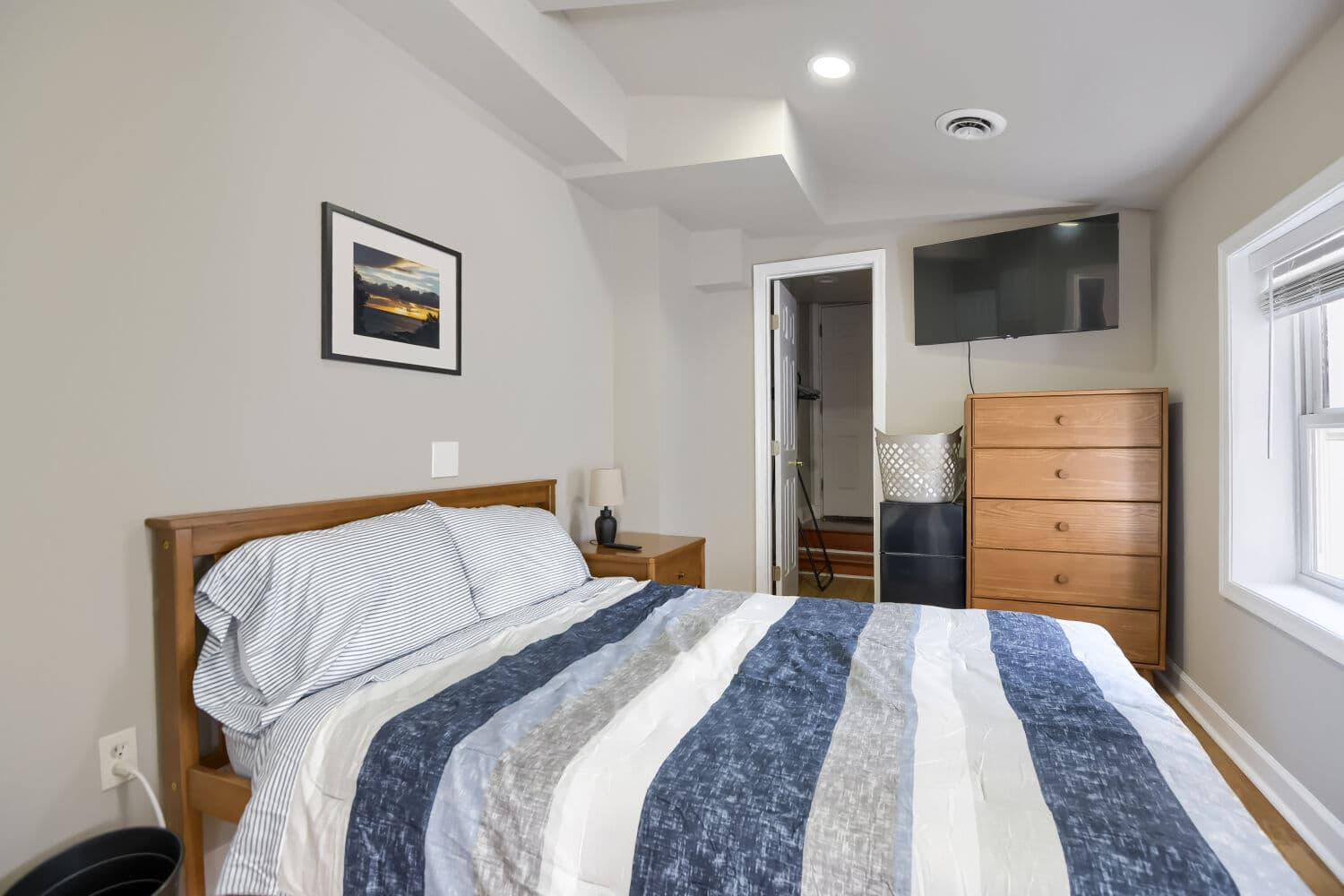 Primary bedroom with queen bed, framed sunset art, wooden dresser, and ensuite bathroom access