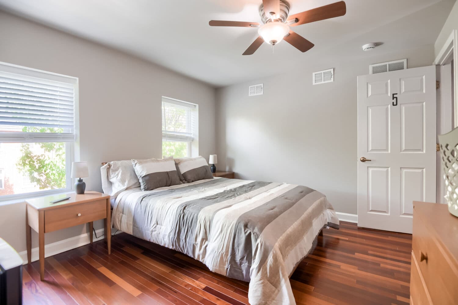 Spacious bedroom with ceiling fan, hardwood floors, and natural light from multiple windows